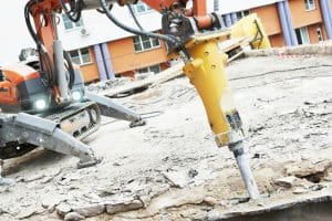 Image of a demolition machine with a hydraulic hammer attachment breaking through concrete on a construction site