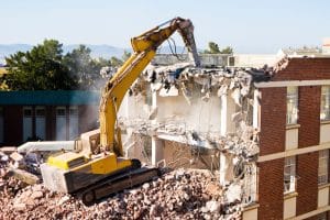 Image of a bulldozer tearing down a brick building with its blade. Demolition machines are used to safely and efficiently remove old structures.