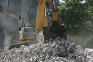 A yellow construction excavator sitting on top of a pile of bricks from a demolition project. Showing a dusty, chaotic demolition site with debris and machinery. Demolition techniques can be used to break down and recycle these materials for future construction projects.