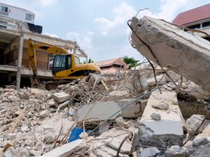 Excavator demolishing a house, clearing debris and rubble on a construction site.