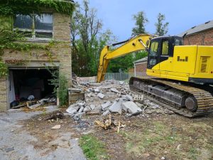 Heavy machinery demolishing a house, removing concrete and brick remains efficiently.