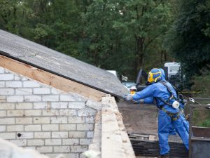 Worker in safety gear removing roofing during a demolition procedure, preparing the house for further teardown.