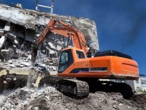 Excavator demolishing a building, revealing different types of foundations beneath the surface.