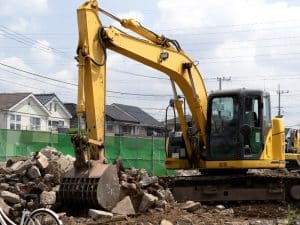 A yellow excavator with its bucket raised, ready for demolition work.