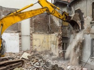 Demolition noise and dust as excavator wrecks a brick building.