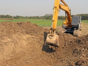 A yellow excavator doing excavation work needed, digging into a large pile of brown earth.