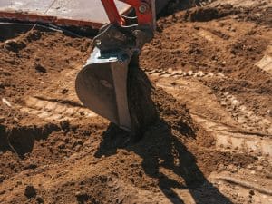 Excavator bucket digging into site during excavation soil removal process.