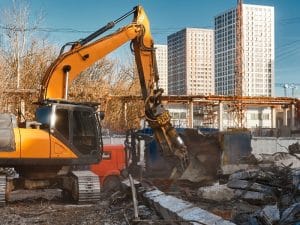 Excavator crushing concrete debris on a construction site, representing small building demolition in urban redevelopment.