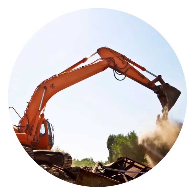 Orange excavator performing demolition by lifting and dropping debris at a construction site under clear sky.