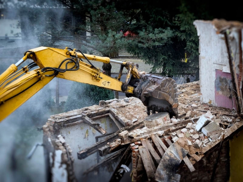 Heavy machinery breaking down brick structure during the house demolition process at an urban site