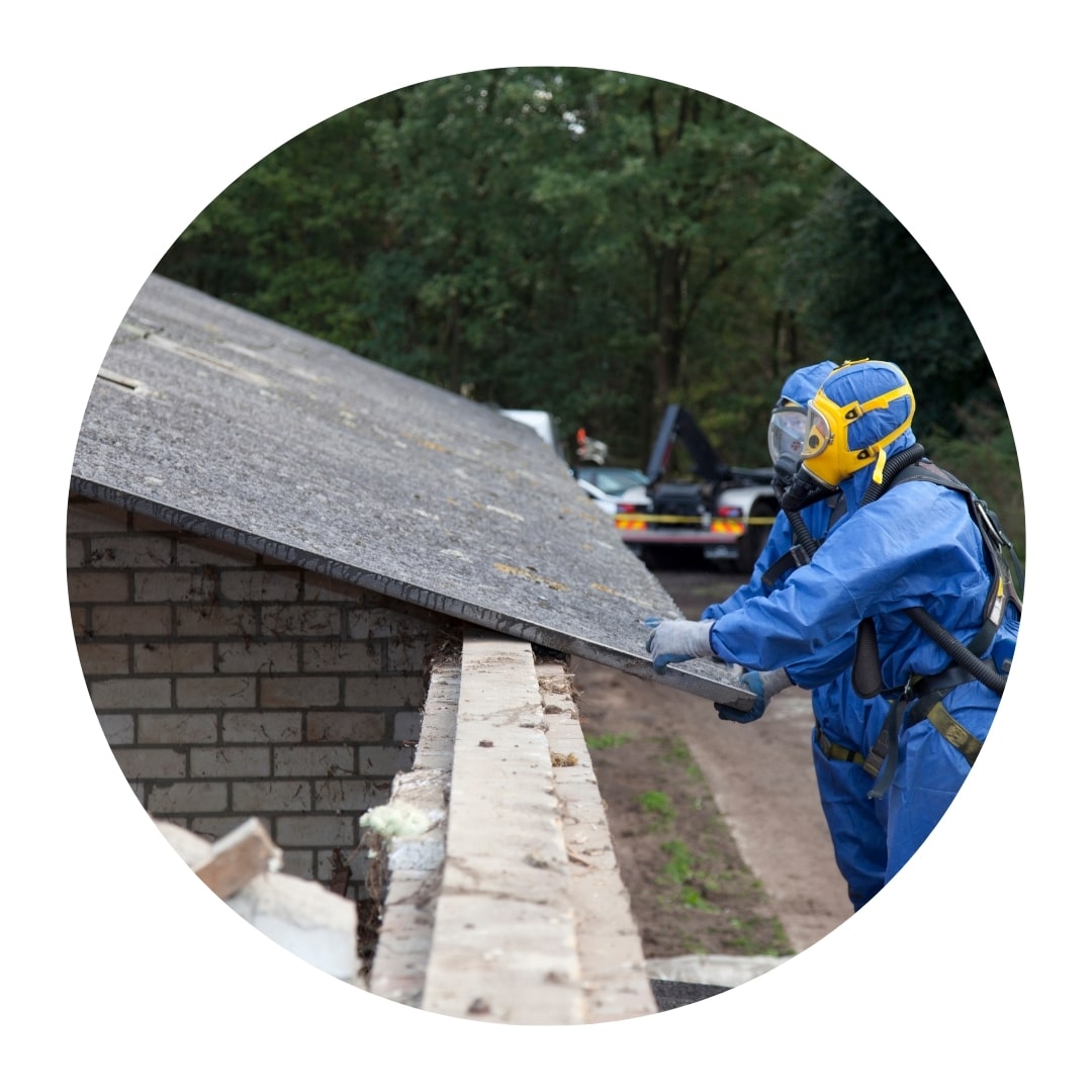 Worker in protective gear removing asbestos roof sheet.