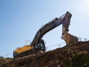 Large excavator positioned on the edge of an excavation site with safety fencing