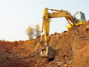 Yellow excavator digging into red soil on a sloped excavation site under clear sky